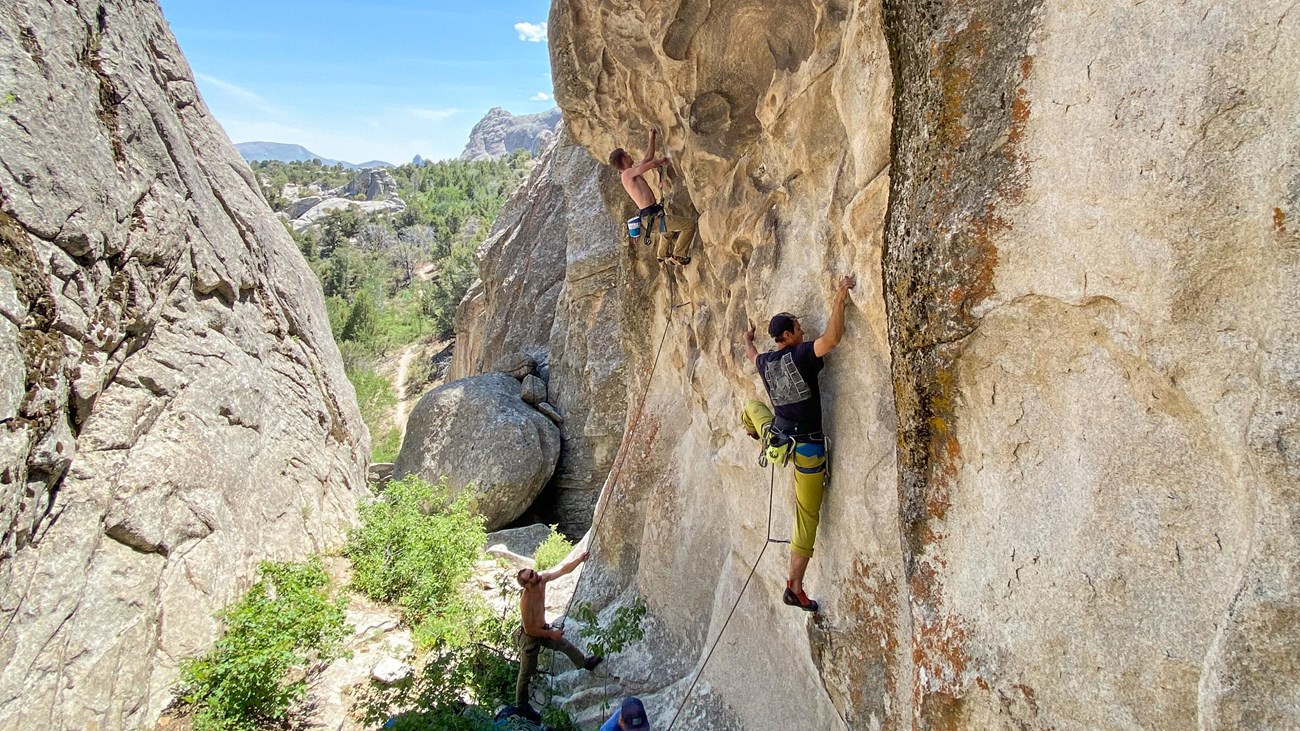 Two climbers ascend neighboring routes in a scenic granite ravine.