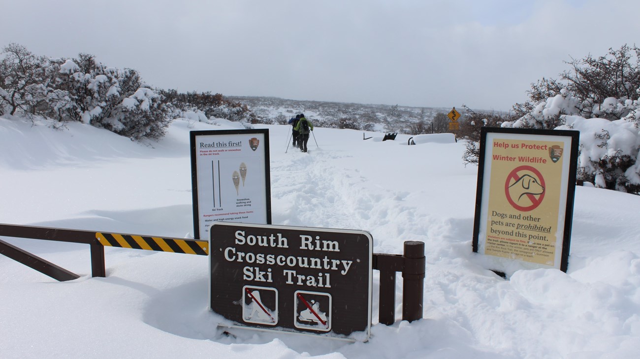 Two large signs behind a gate where people can cross-country ski