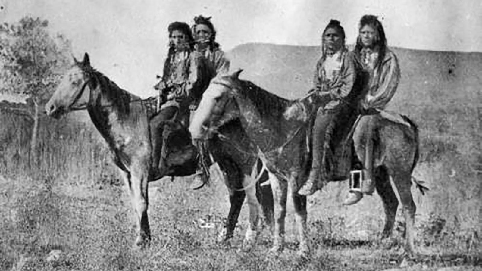 Photo of four Shoshone men riding two horses.