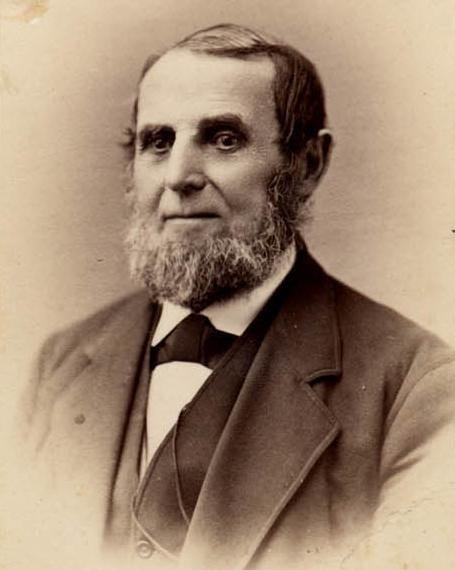 White man with a graying beard and a dark three-piece suit.  