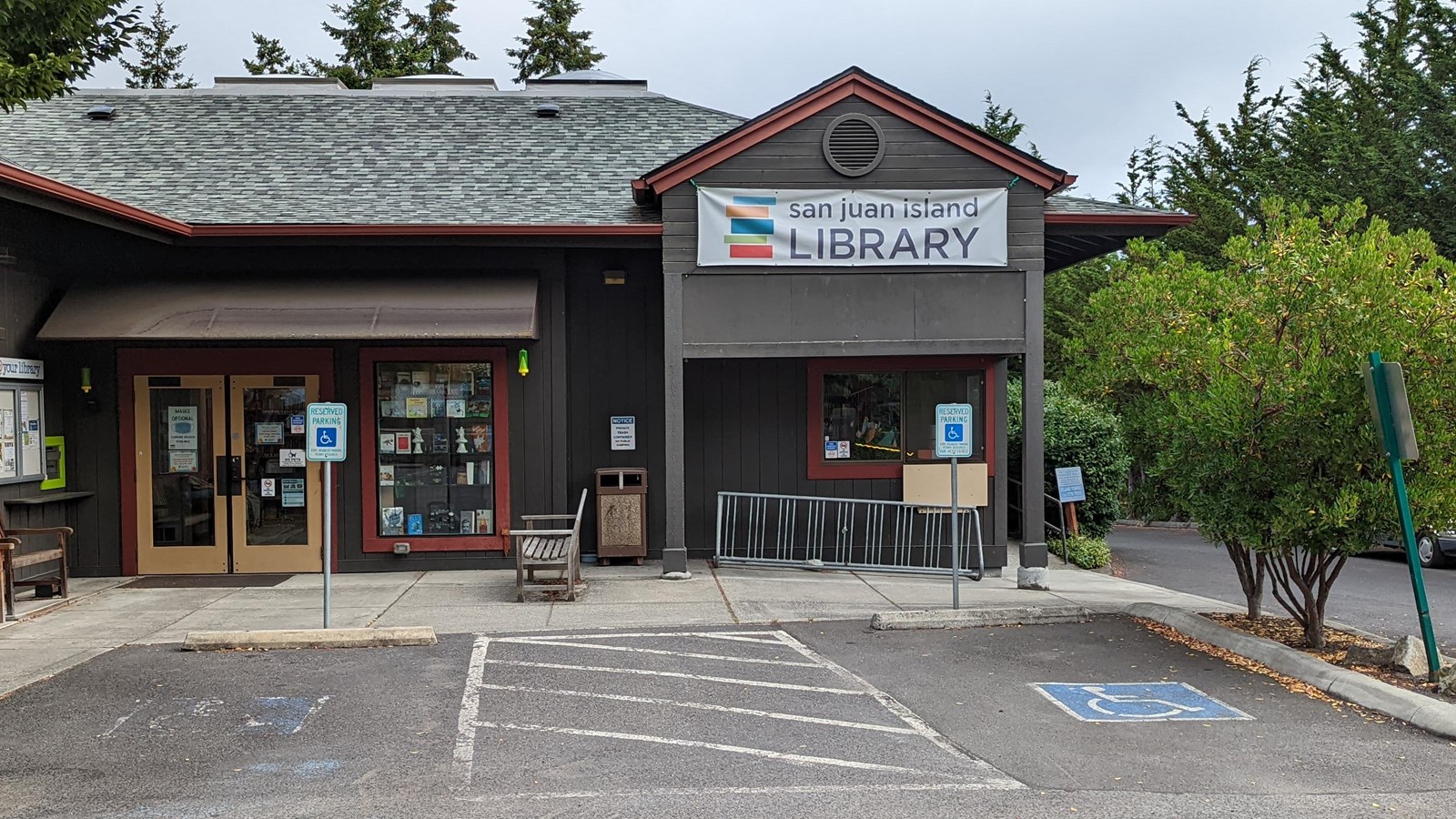 A building entrance with signage, benches, and parking