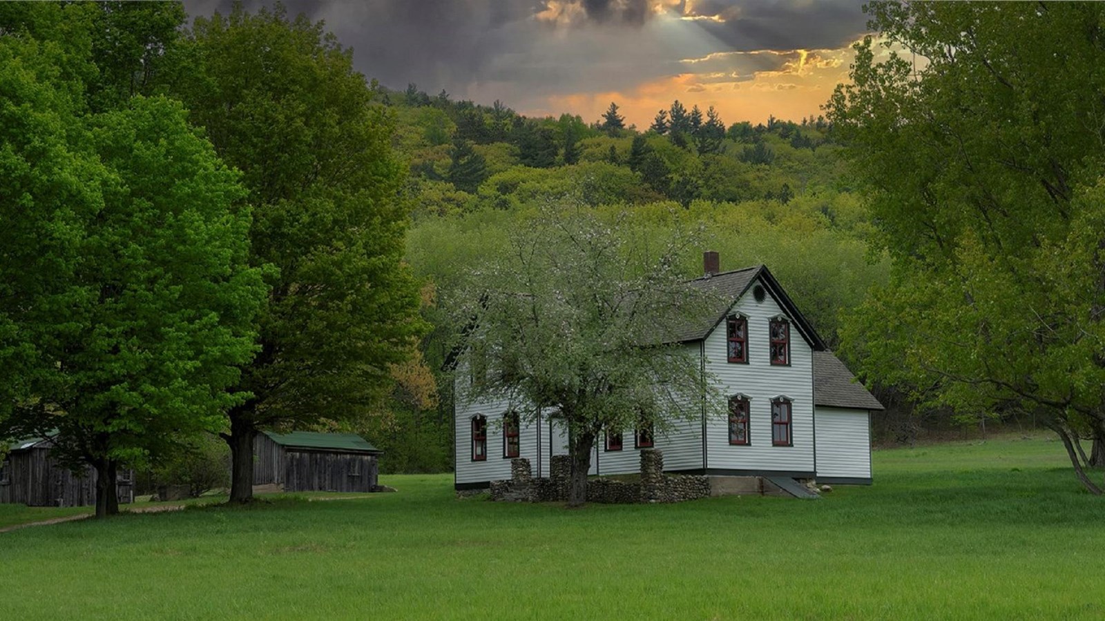 A cloudy sky glows over a farm, with a white two-story farmhouse, tall apple tree, and outbuildings