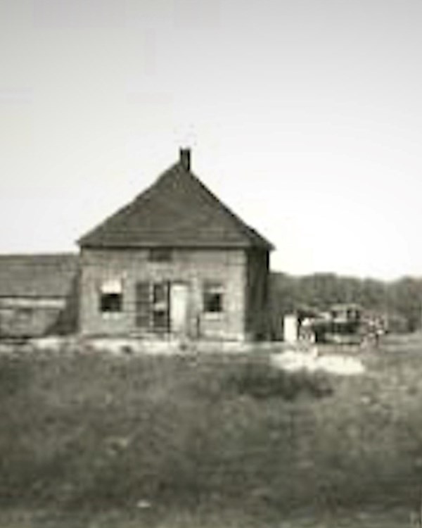 Black and white photo of small one room home with early 1900's vehicle outside.