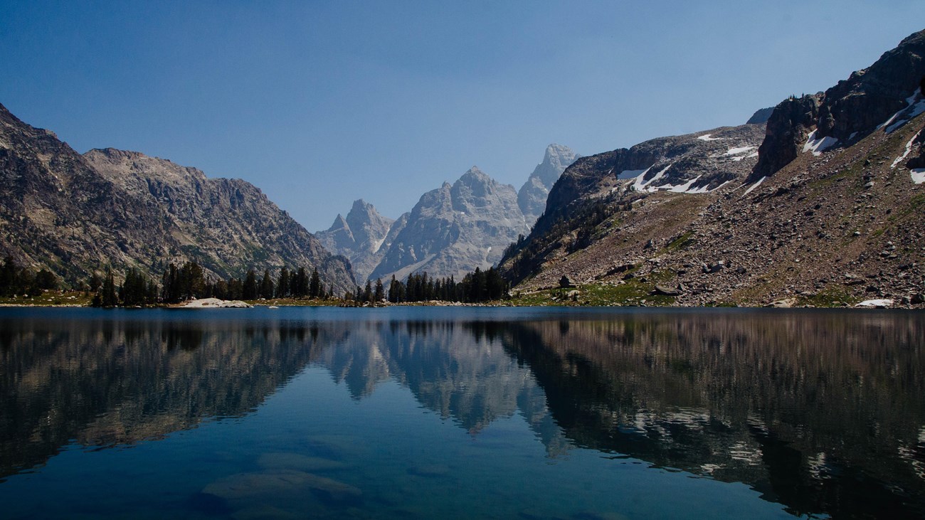 A small lake surrounded by mountains reflects the mountainous scenery on its calm surface.