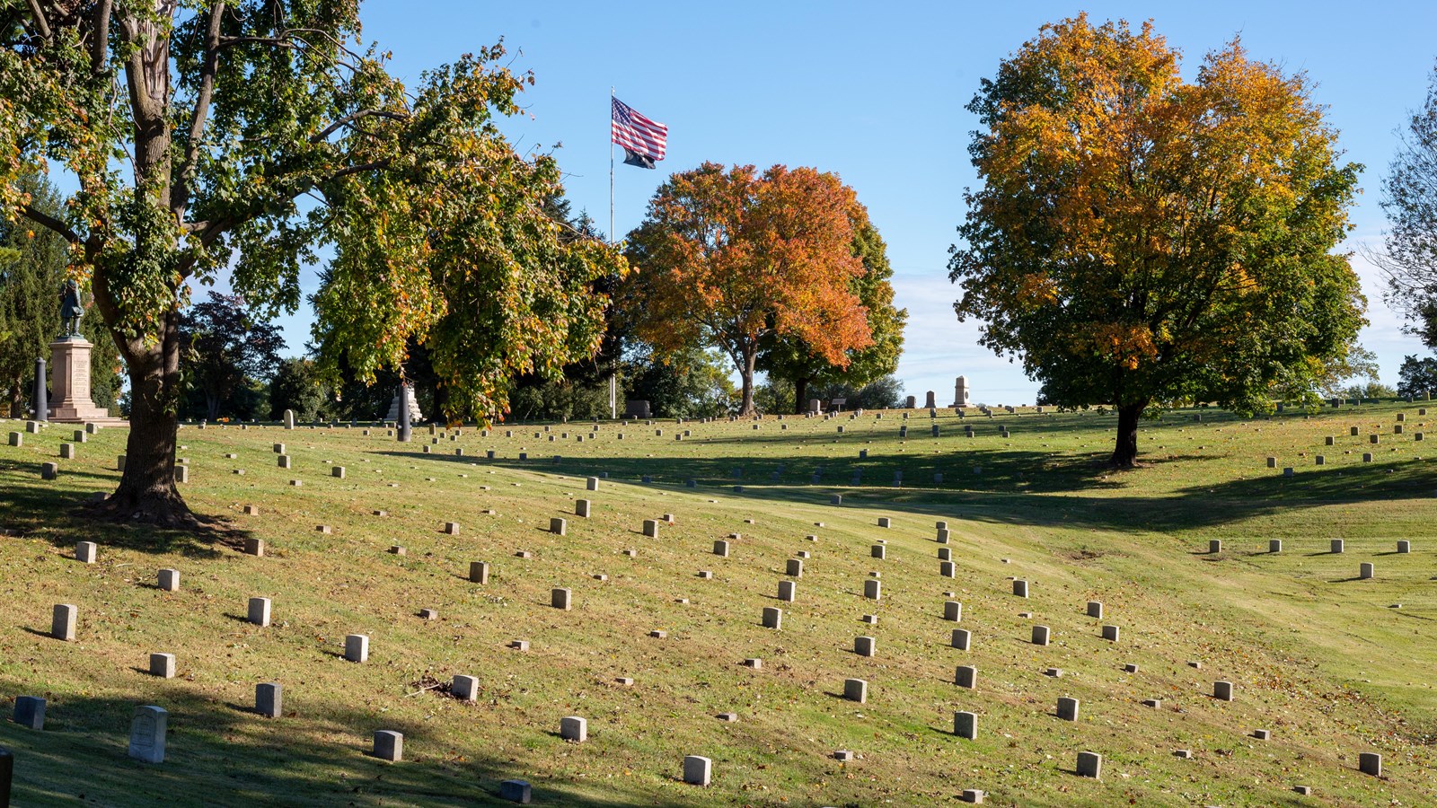 A cemetery with rolling hills, American flag in the distance,
