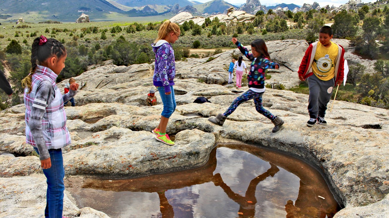Kids play around a water filled depression on a granite slab formation.