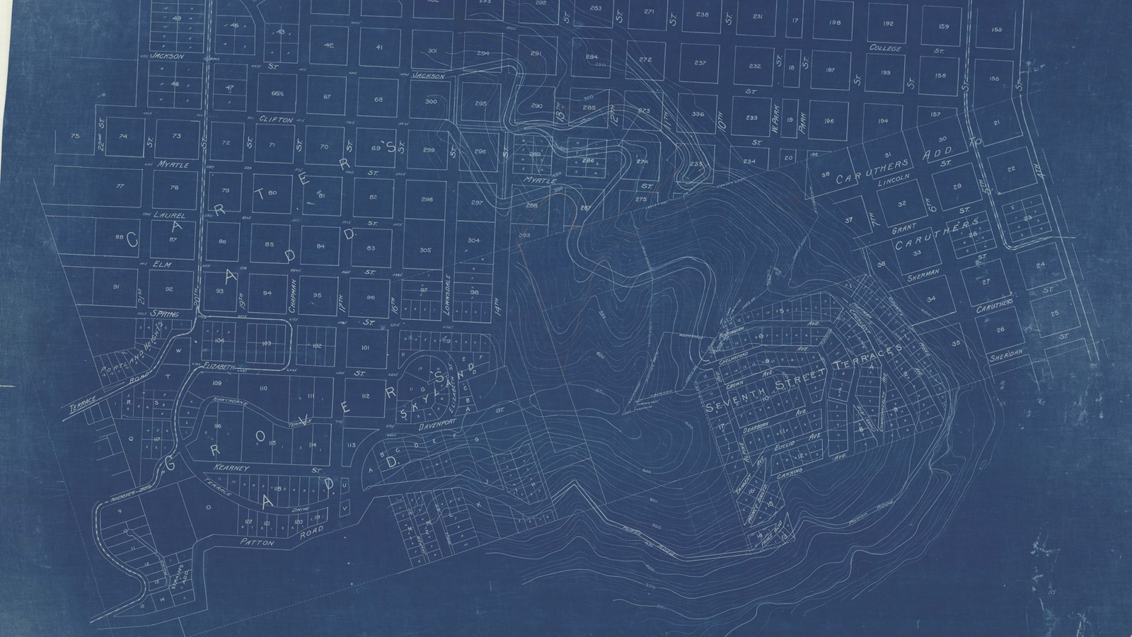 Blueprint of city with straight lined streets and lots for building, with hilly area on edge 