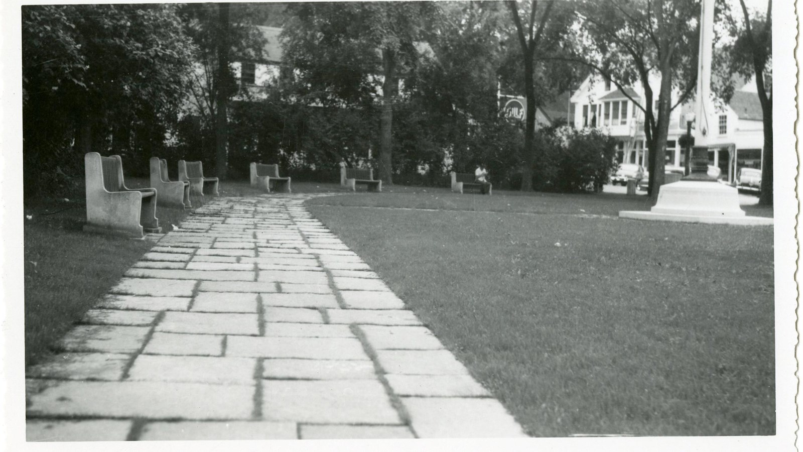 Black and white of brick path curving through grassy area with benches lining one side