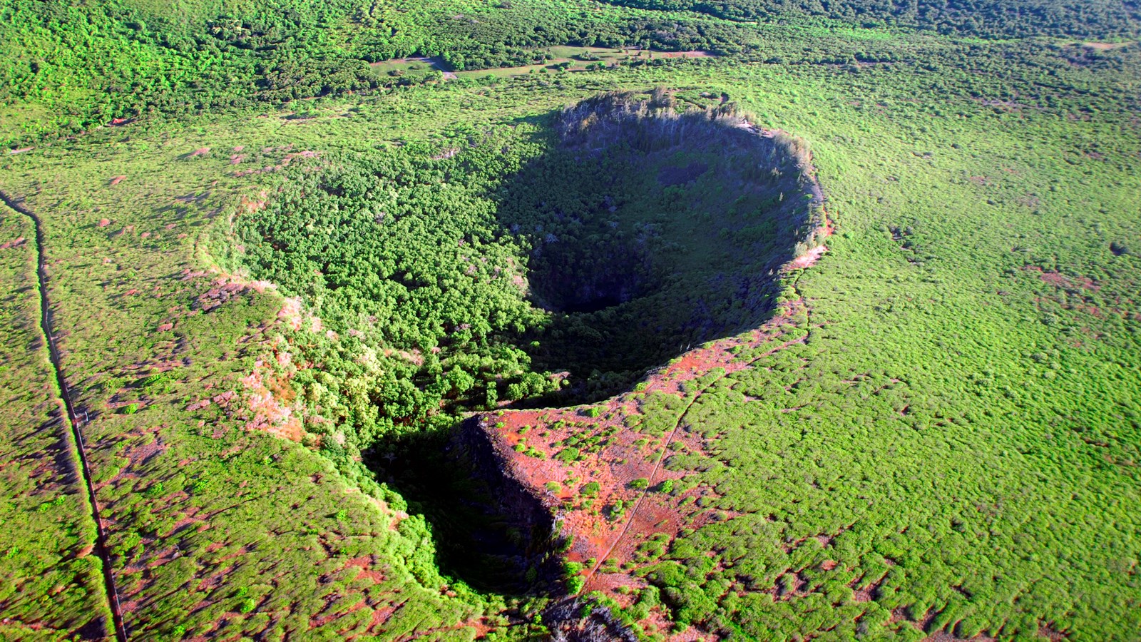 An aerial view of a crater with green vegetation growing over it. 