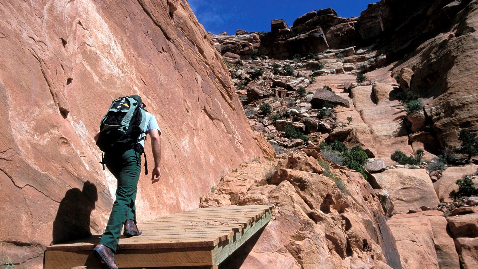 A hiker steps up onto a wooden bridge to ascend a steep canyon trail
