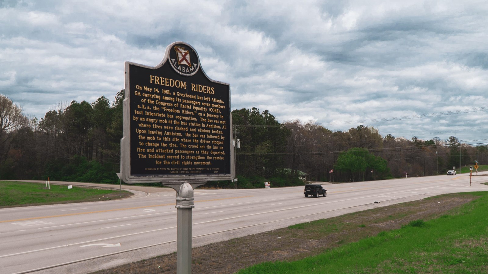 A sign reading Freedom riders made of metal is in the foreground. A highway runs in the background.