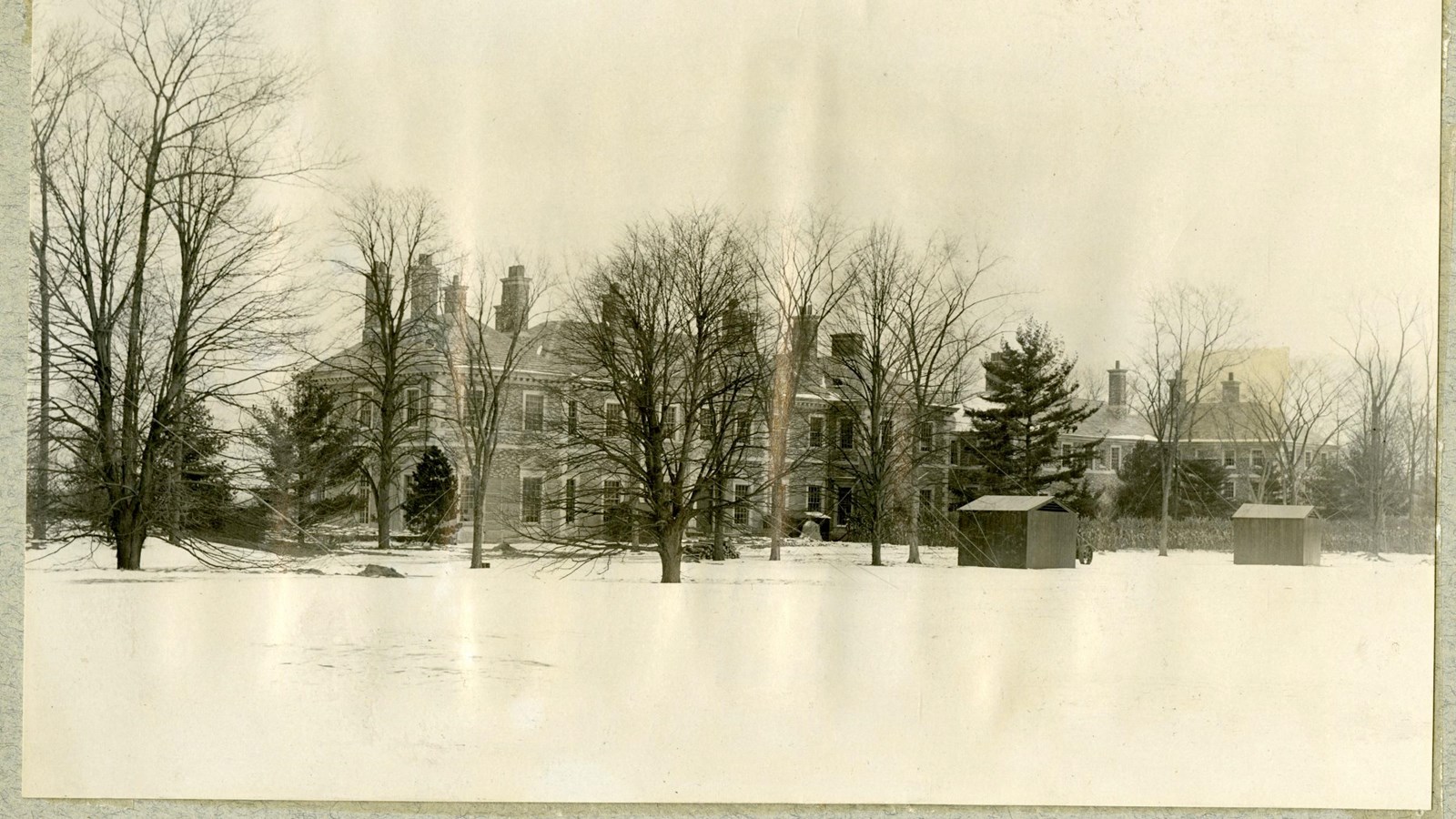 Black and white of large home with trees in front and snow on the ground