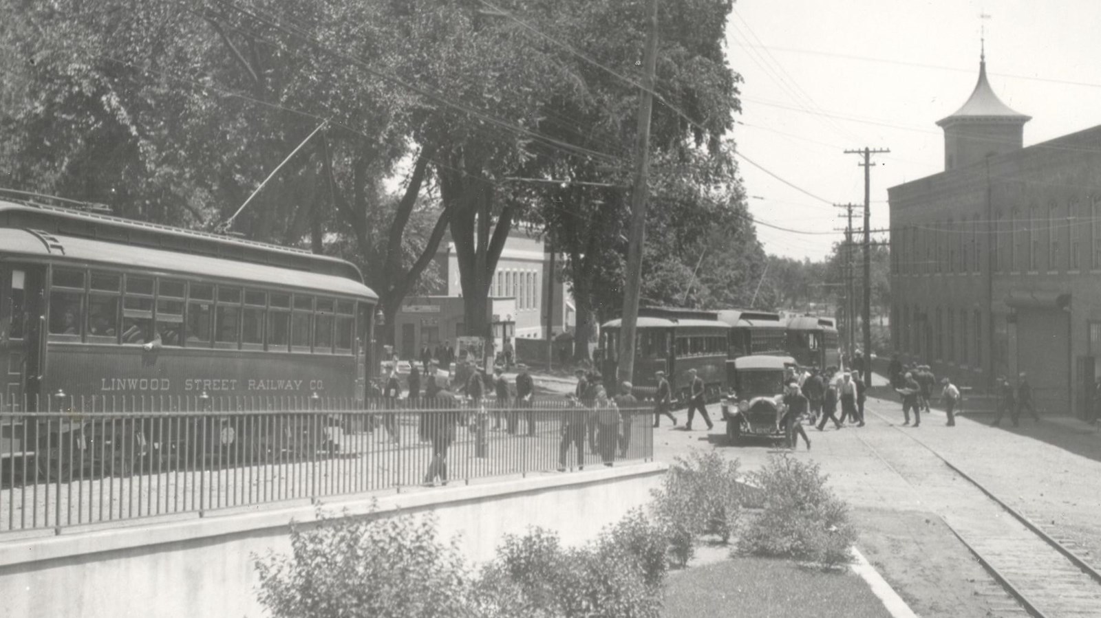 Workers leaving mill at the end of shift. Trolleys on left side of image and mill on the right