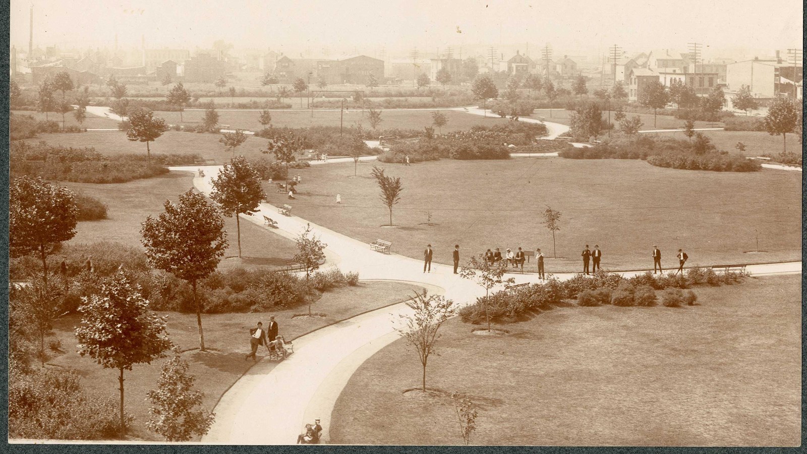 Black and white of park with curving path through grassy space with people walking on it and trees