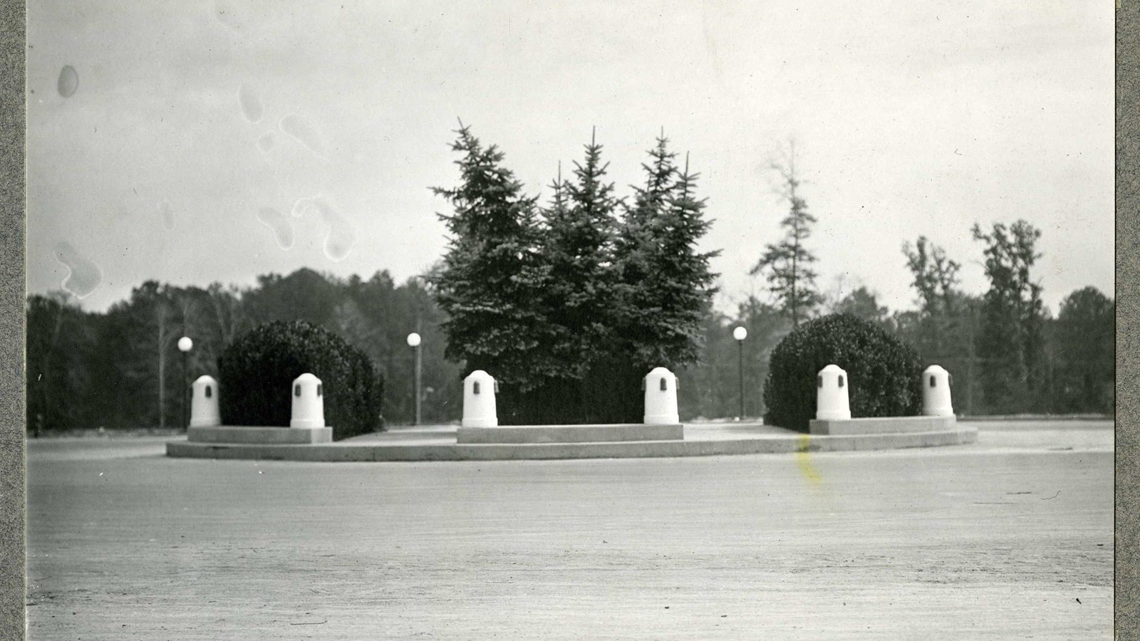 Black and white of road with grass circle and white stones on it with trees behind