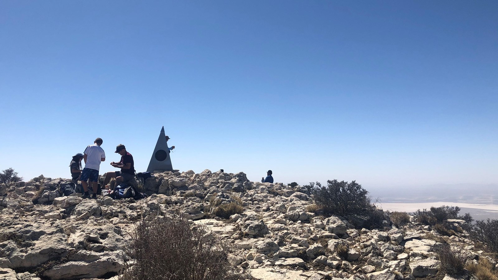 groups of people sit and stand on a stony summit. 