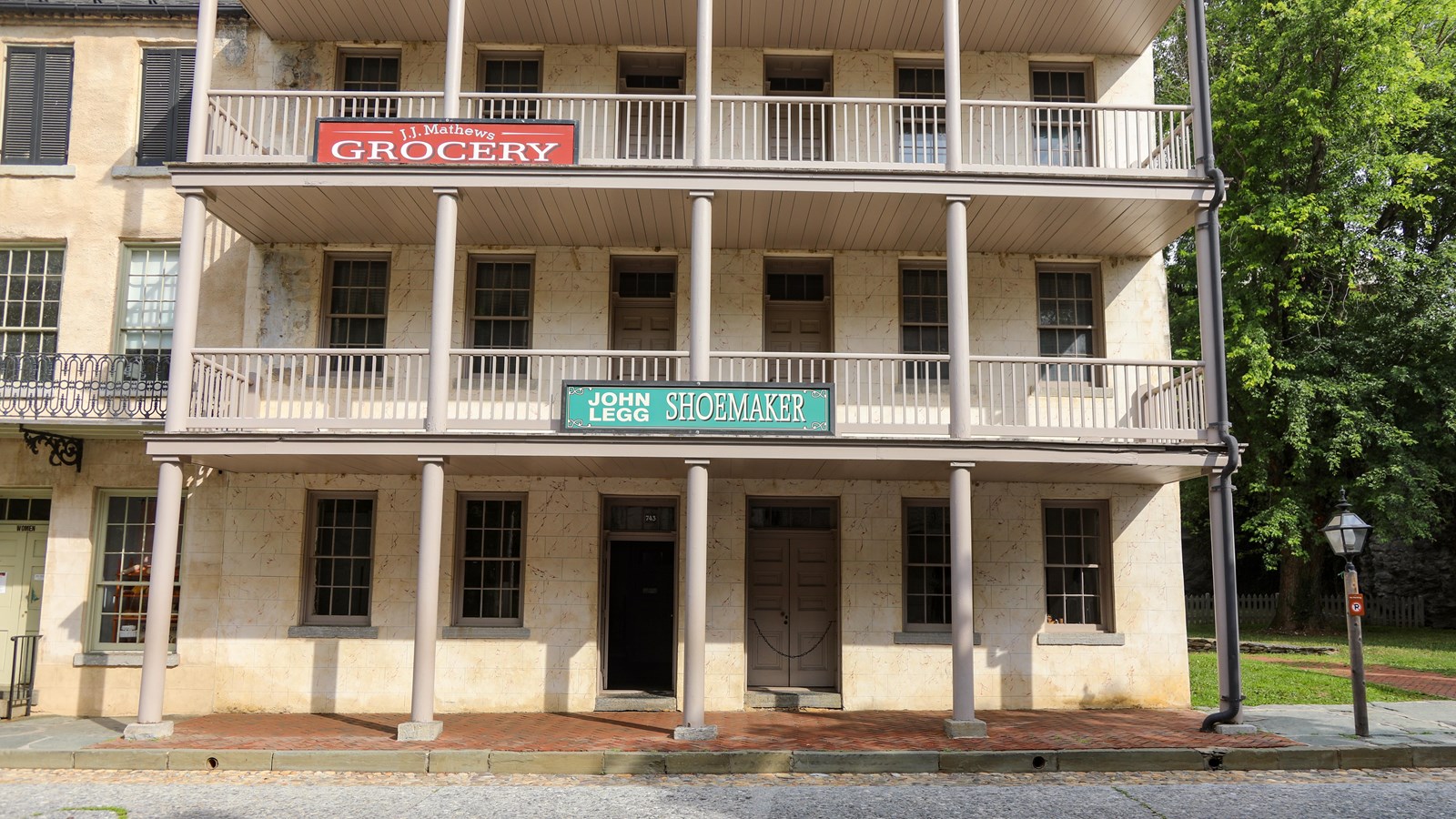 A three-story cream-colored building with balconies and signs for shoemaker and groceries.