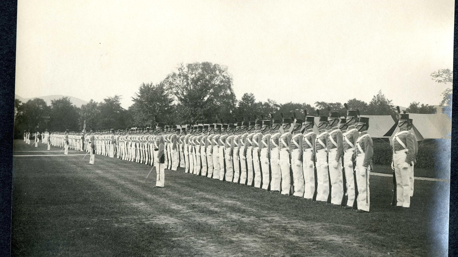 Black and white of soldiers in same uniform standing in straight line on flat grassy area