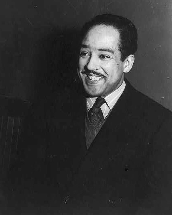 Head and shoulders portrait of Langston Hughes laughing in a suit.