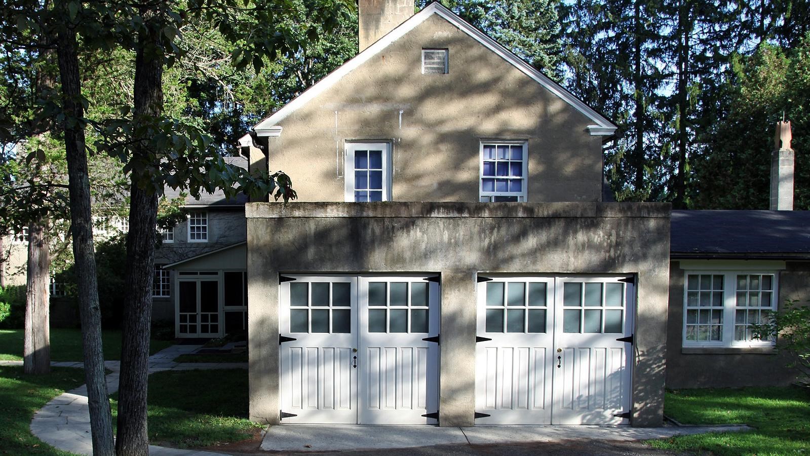 A rambling stucco two story cottage with a pair of double garage doors.