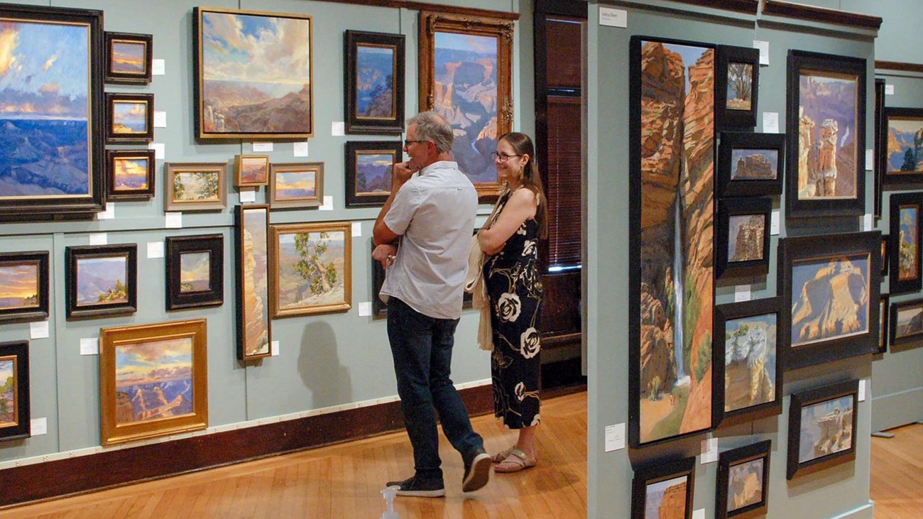 Colorful Grand Canyon paintings of different sizes hanging on walls in an art gallery. 