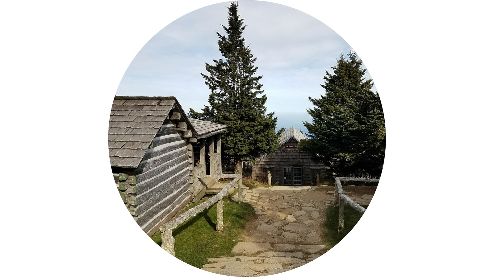 Wooden cabins surrounded by trees and grass, with a mountain view in the distance.