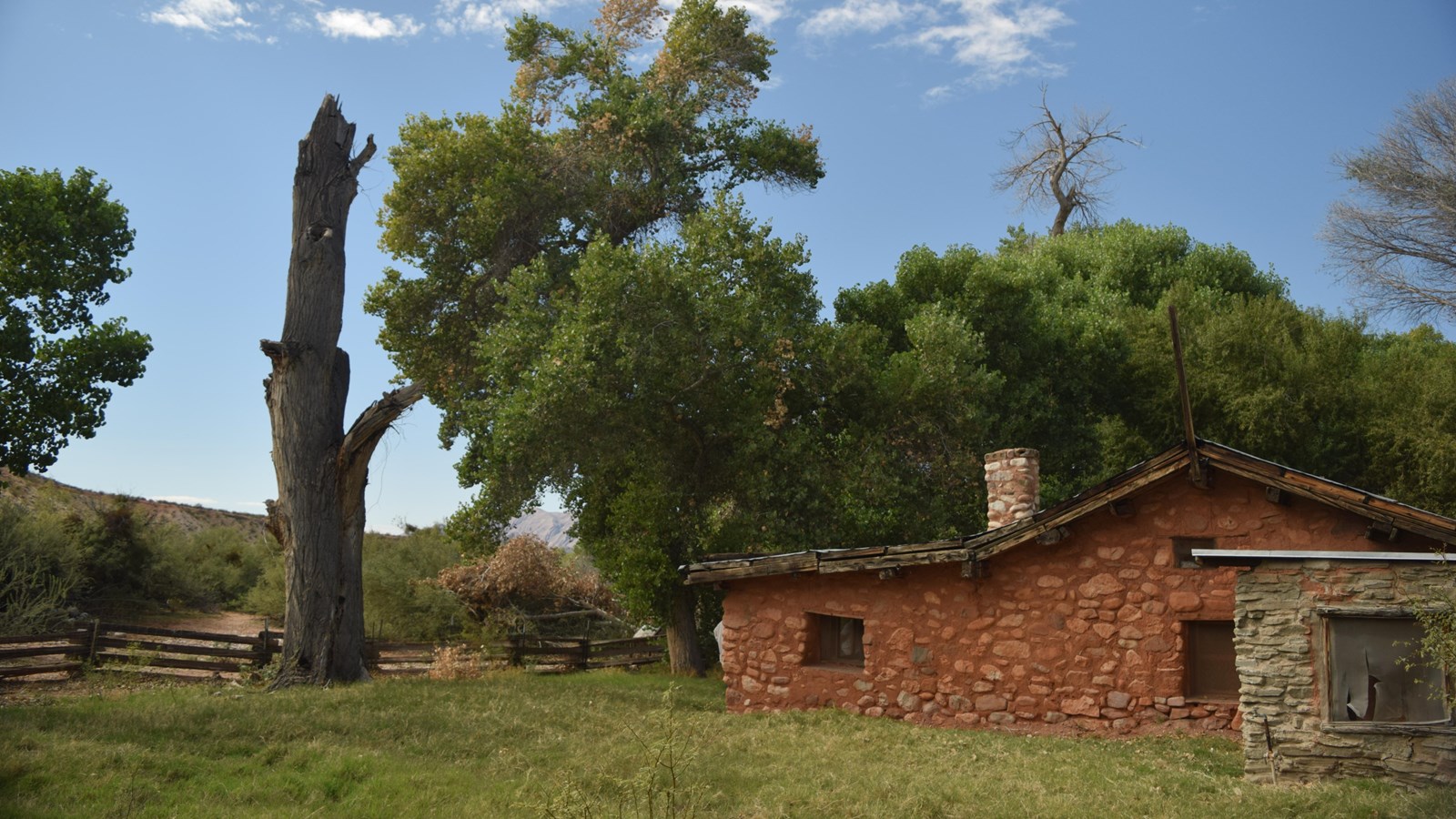 A rusty colored house made of rock with large cottonwood trees surrounding it. 