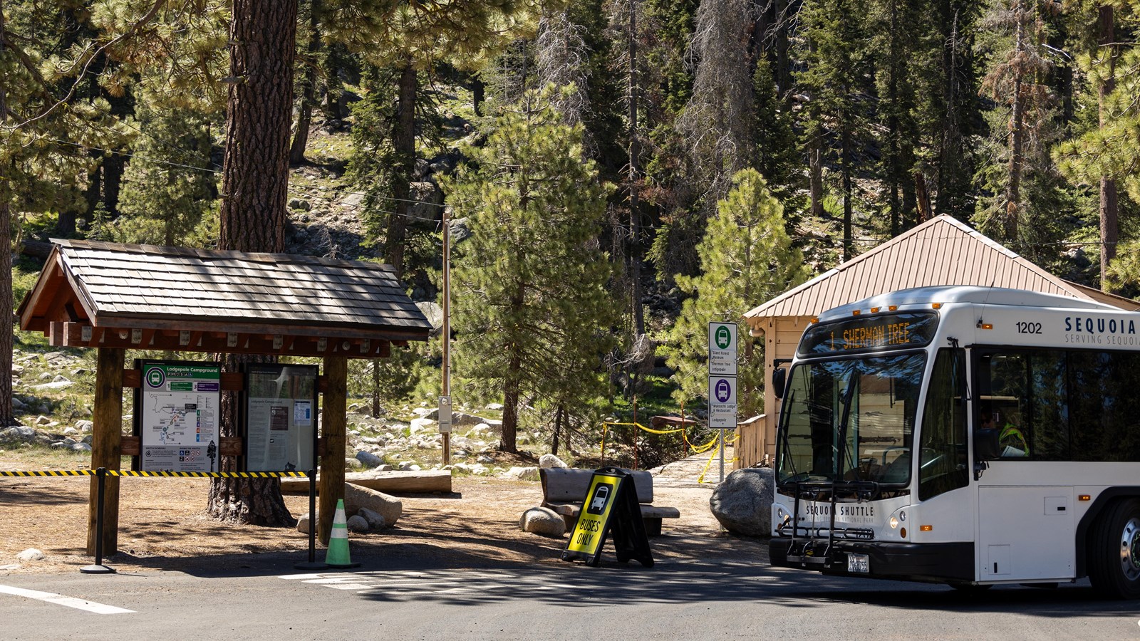A white shuttle bus is parked next to a wooden kiosk labeled