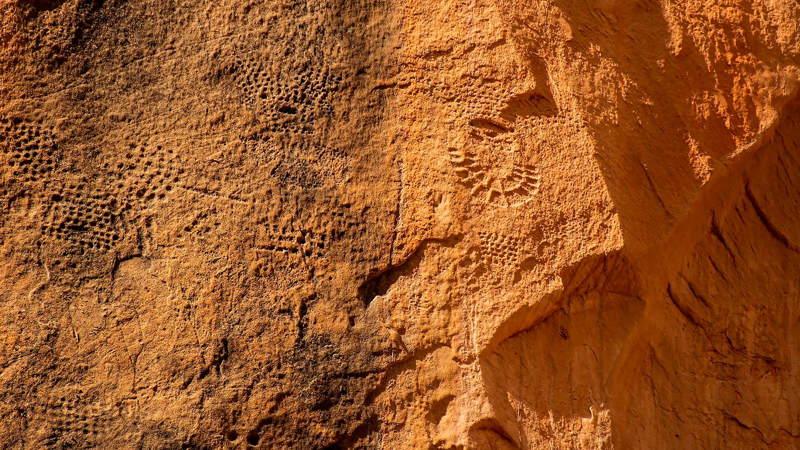 A series of organized holes and etchings form images in the rock face.