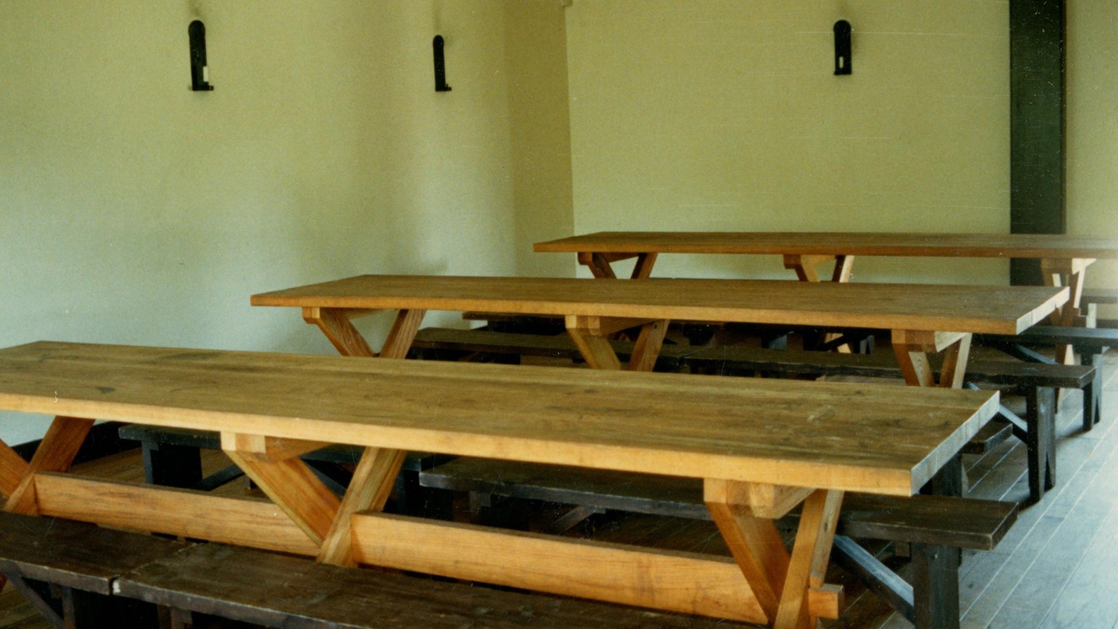 Long wooden tables and benches in square room.