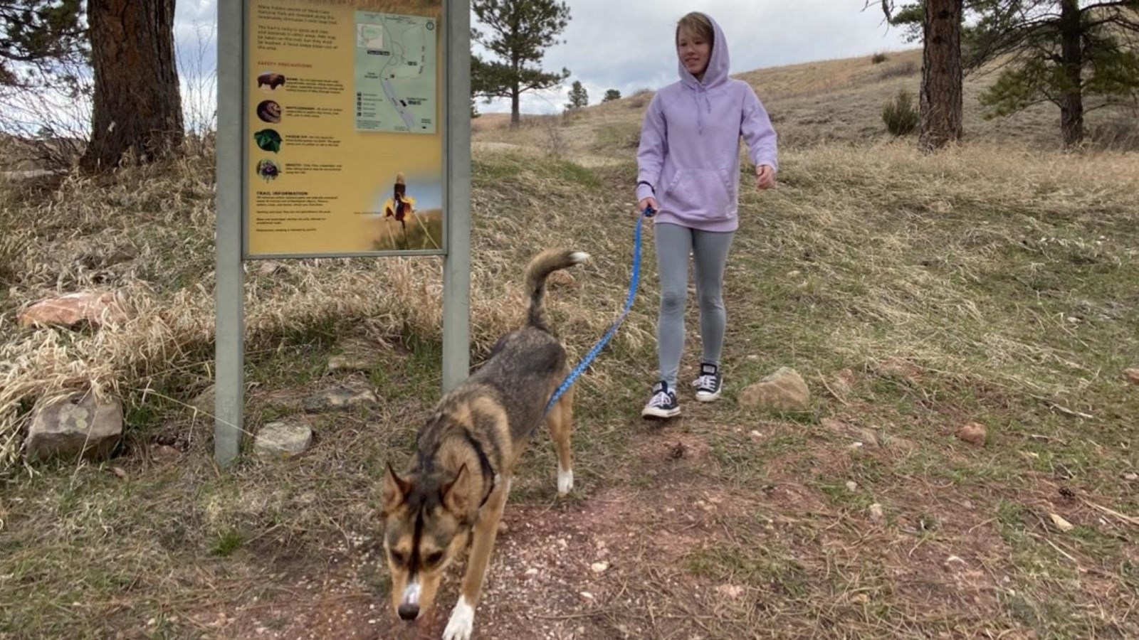 A visitor walks their dog with the Prairie Vista trailhead sign in the background. 