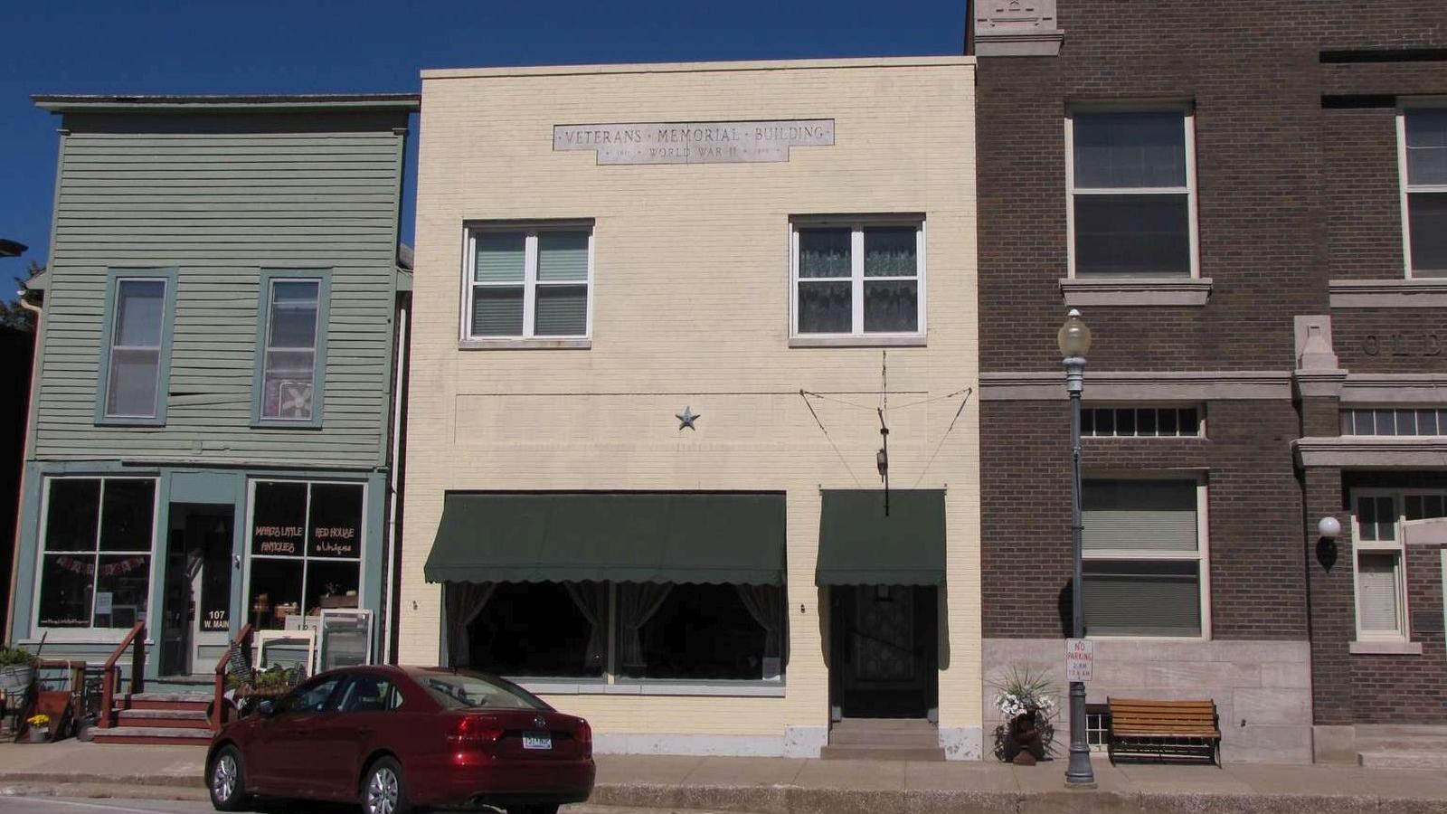 A flat-roofed downtown building is painted cream and has a green awning on the first floor.