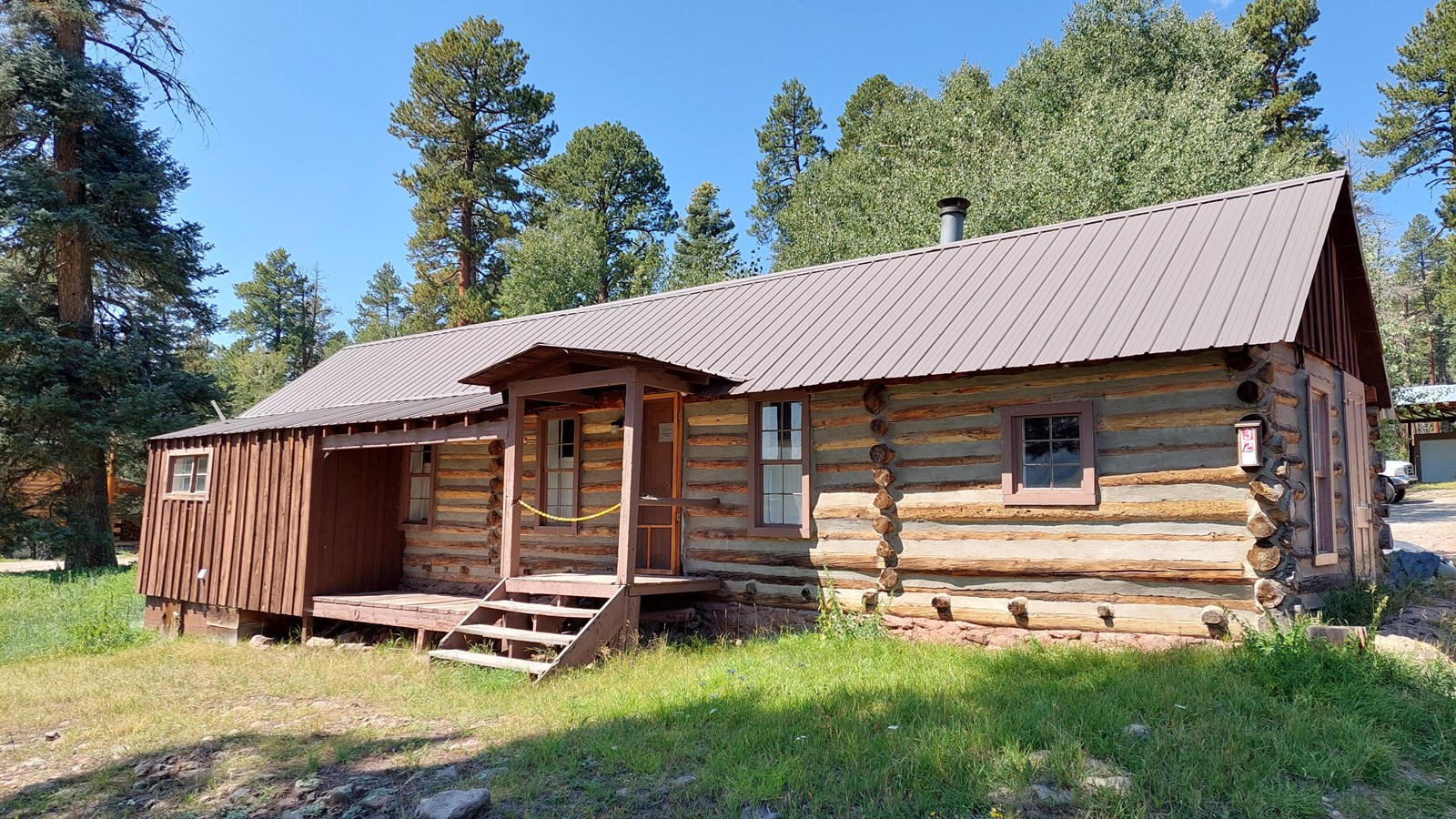 A long, brown and tan wooden cabin with trees in the background.