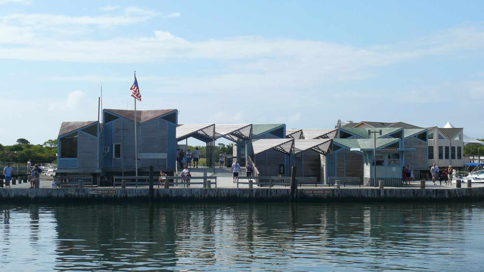 An assortment of short angular buildings stand on a dock above a calm body of water. 