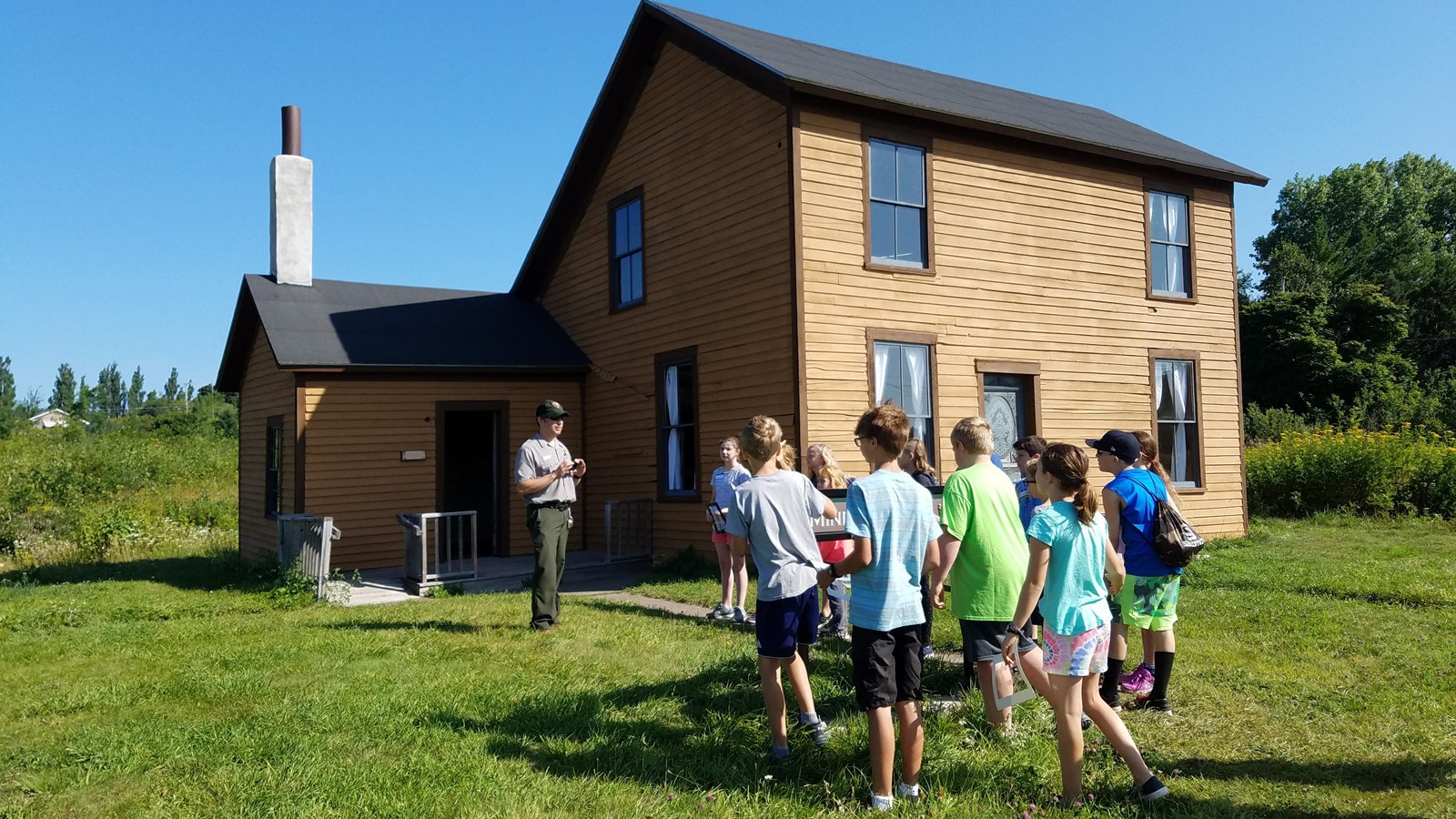 A park ranger speaks to a group of kids in front of a company house.