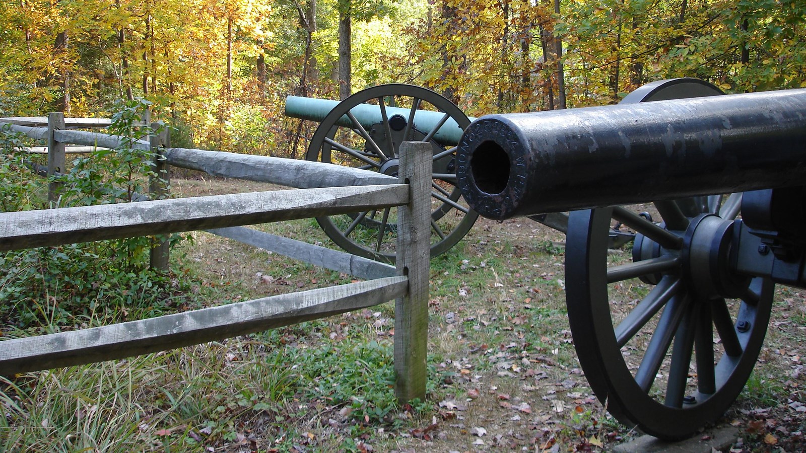 A cannon in front of a wood fence pointed to a field.