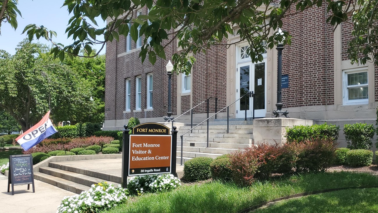 Signs in front of a brick Beaux-Arts style building state that the visitor center is open. 