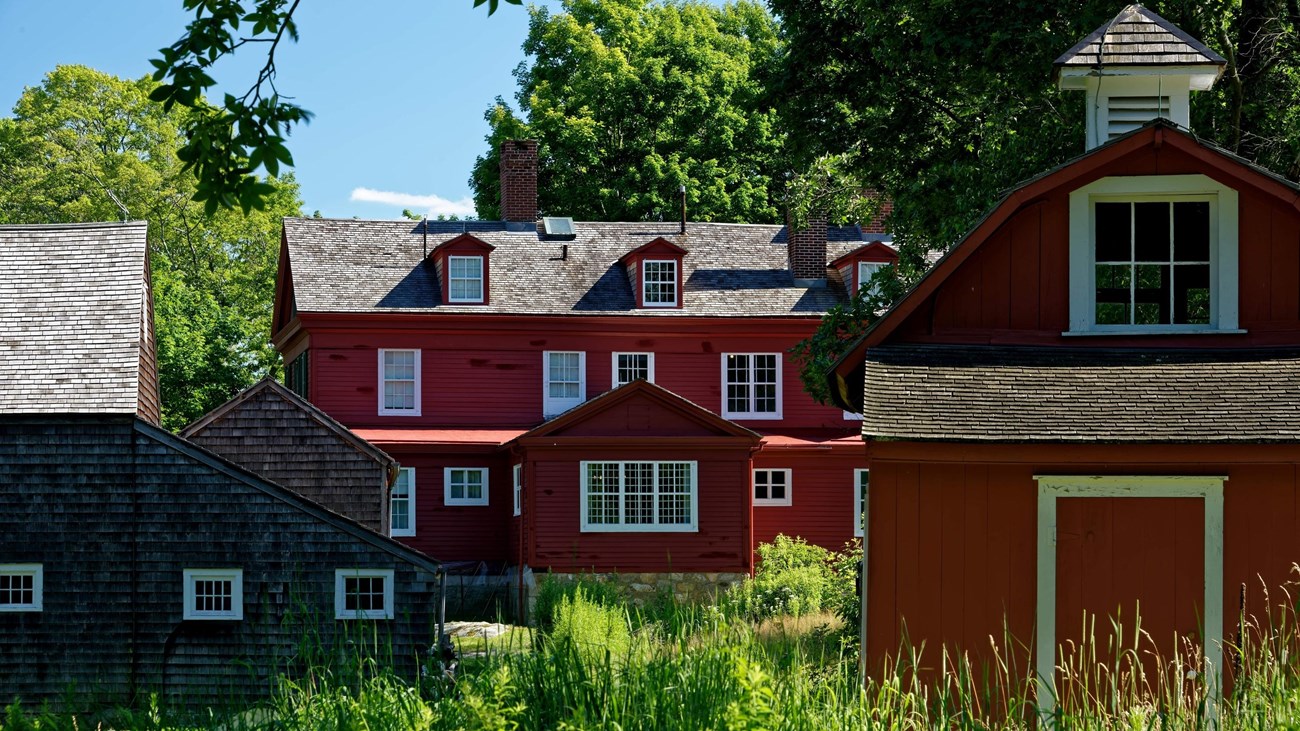 A back of a red house with two other buildings in front of it.