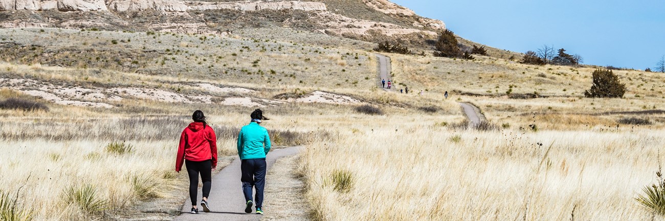 Two hikers walk towards an interesting rock formation.