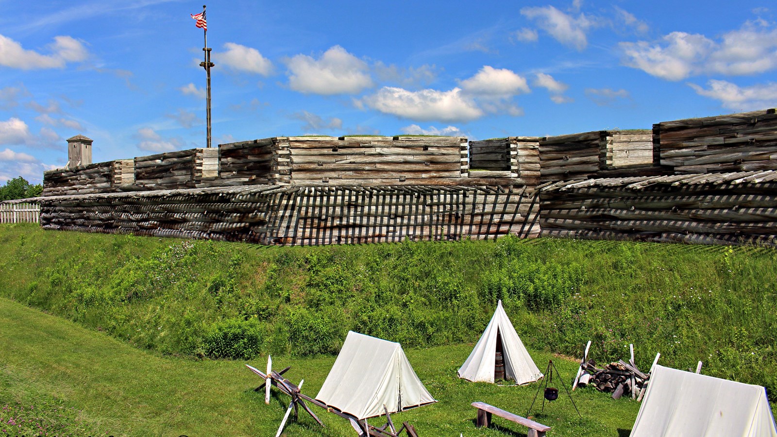 In a ten foot deep, ten foot wide, grassy trench, you can see three canvas tents and the fort wall. 