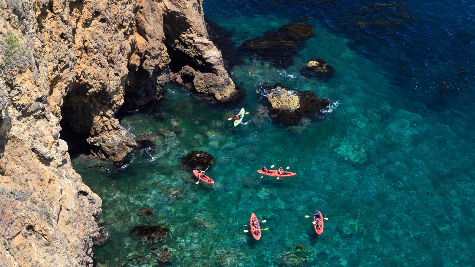 group of kayakers in clear ocean water near cliff.