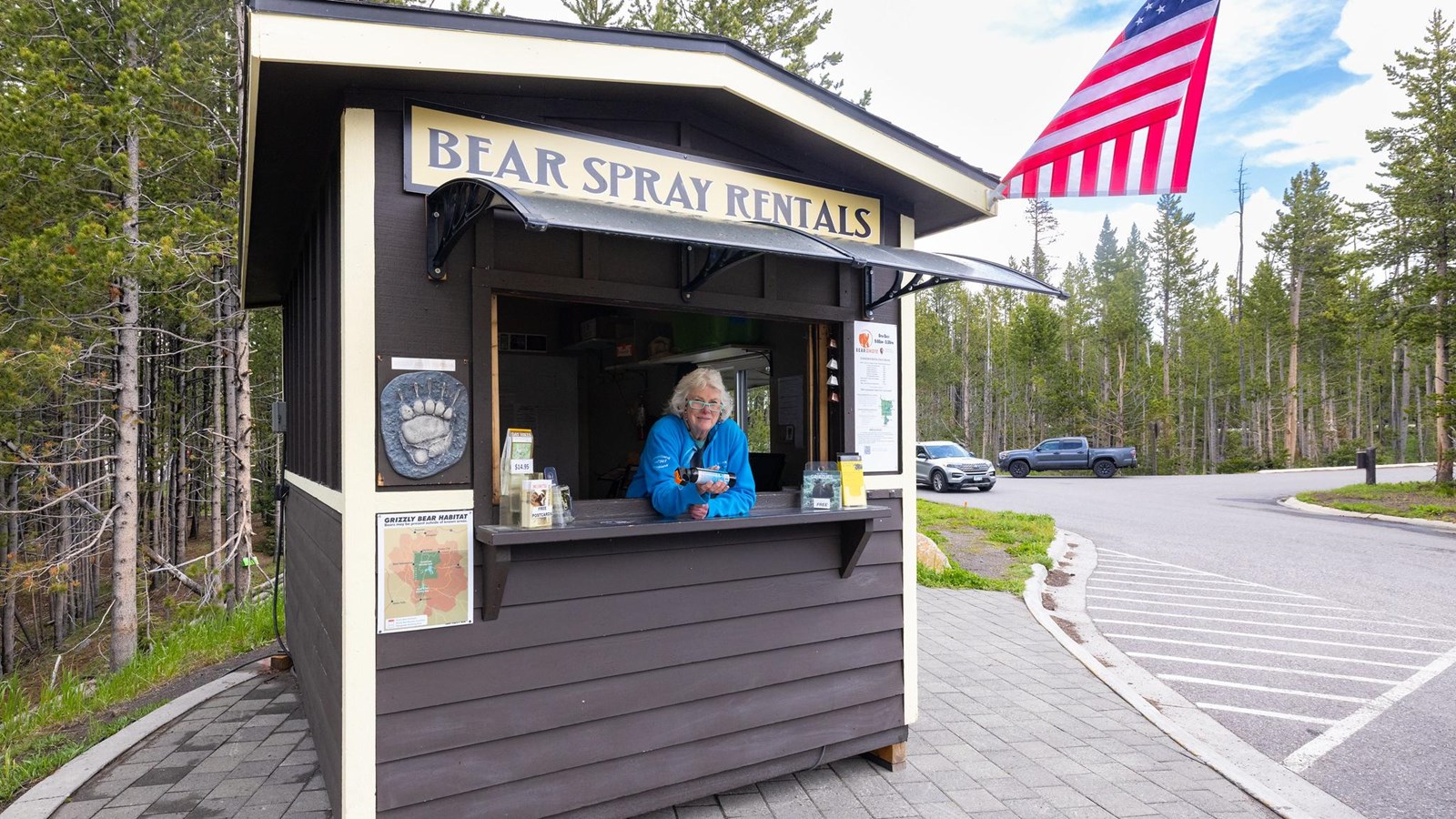 An employee leans out the window of a bear spray rental kiosk with a can of bear spray.
