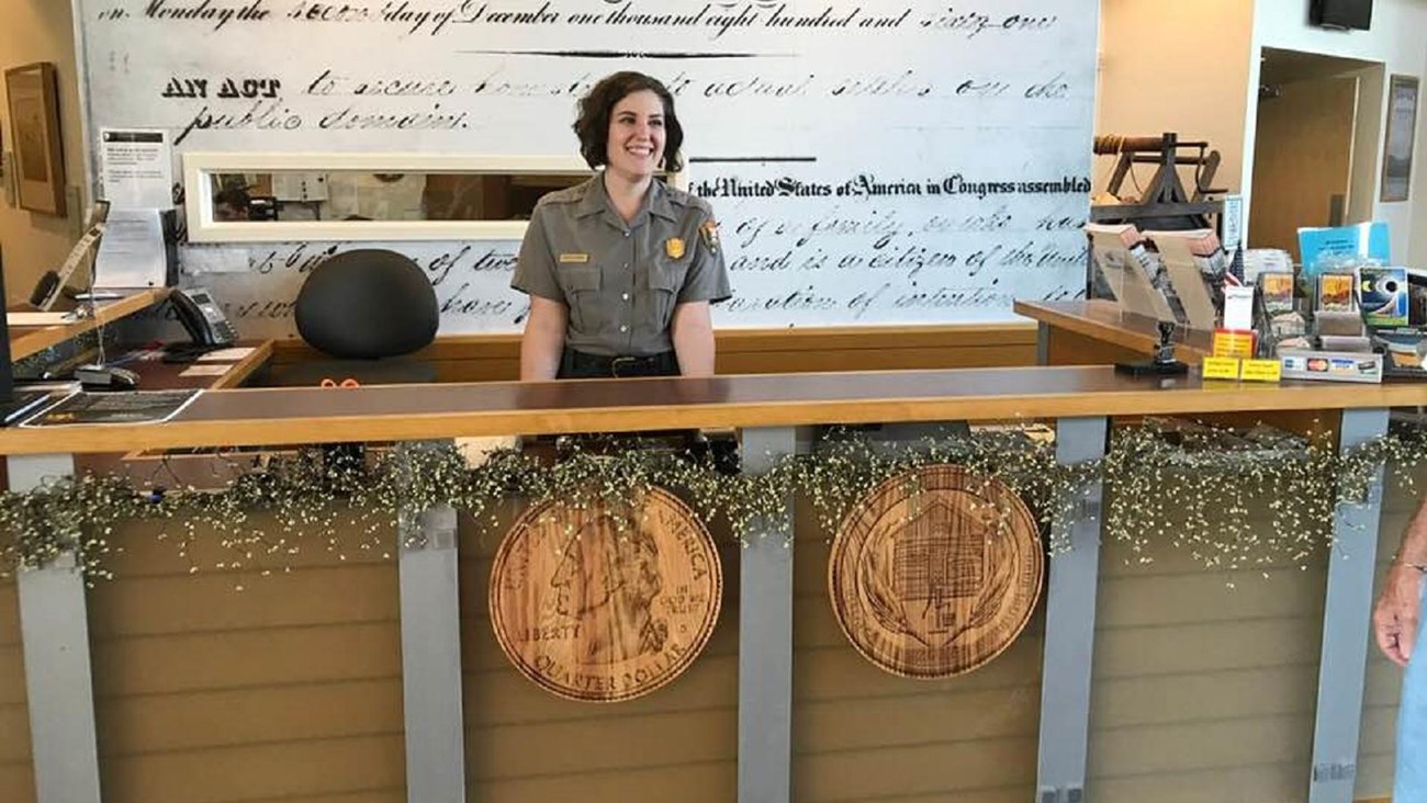 A ranger smiles standing behind an information desk.