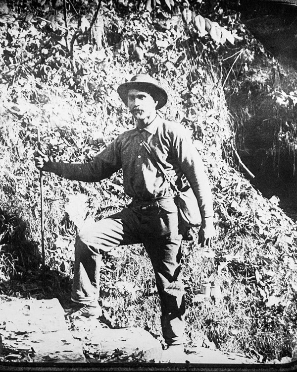 A black and white photograph of a man standing near the cave entrance.