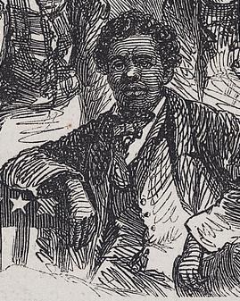 A man sits in a suit with one arm leaning on a table with and American flag.