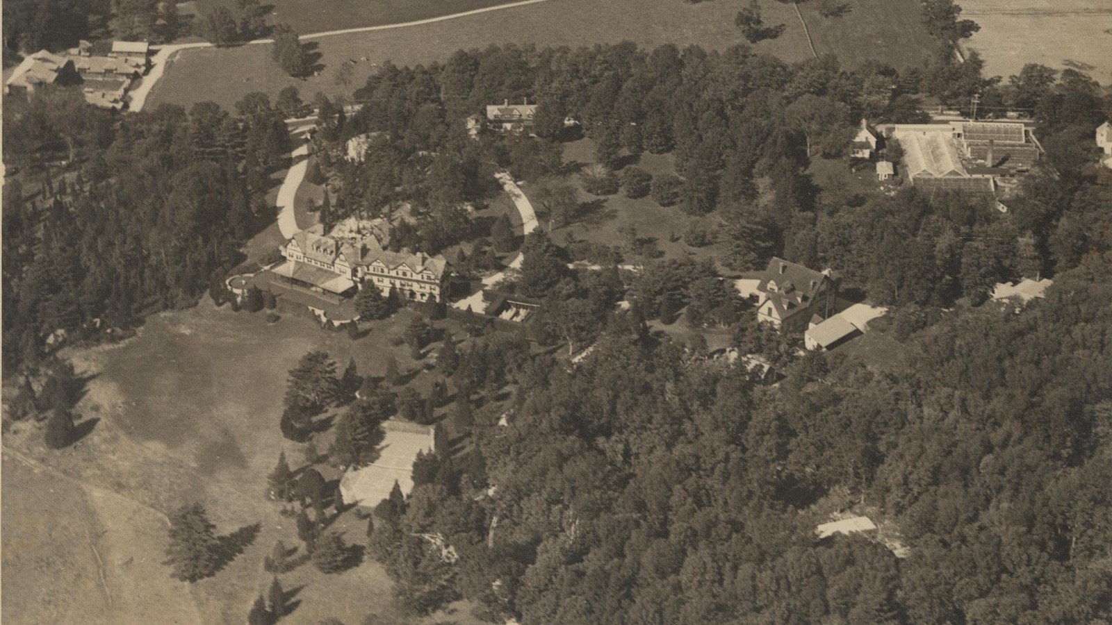 Black and white aerial of large estate with lots of trees and little open space in front