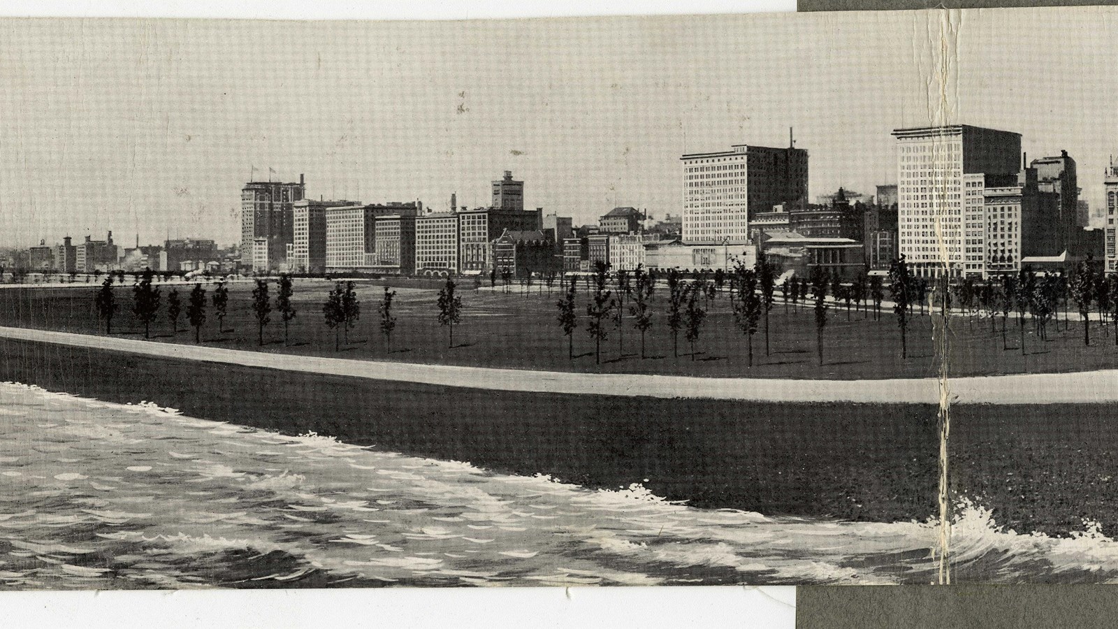 Black and white of flat grassy area with path going in circle around it with buildings in back