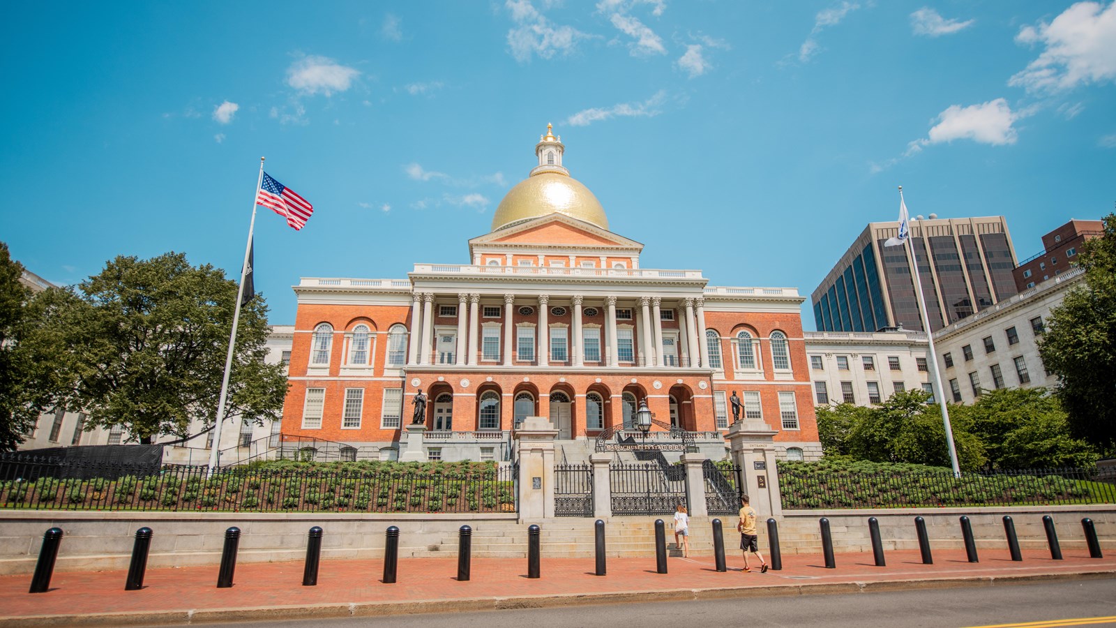 Red brick and white trimmed State House with a gold dome against a blue sky.