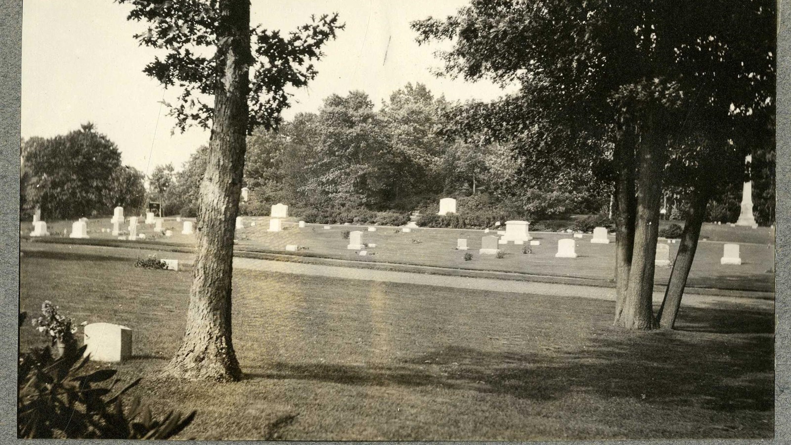 Black and white of flat grassy area with white tombstones and some trees 