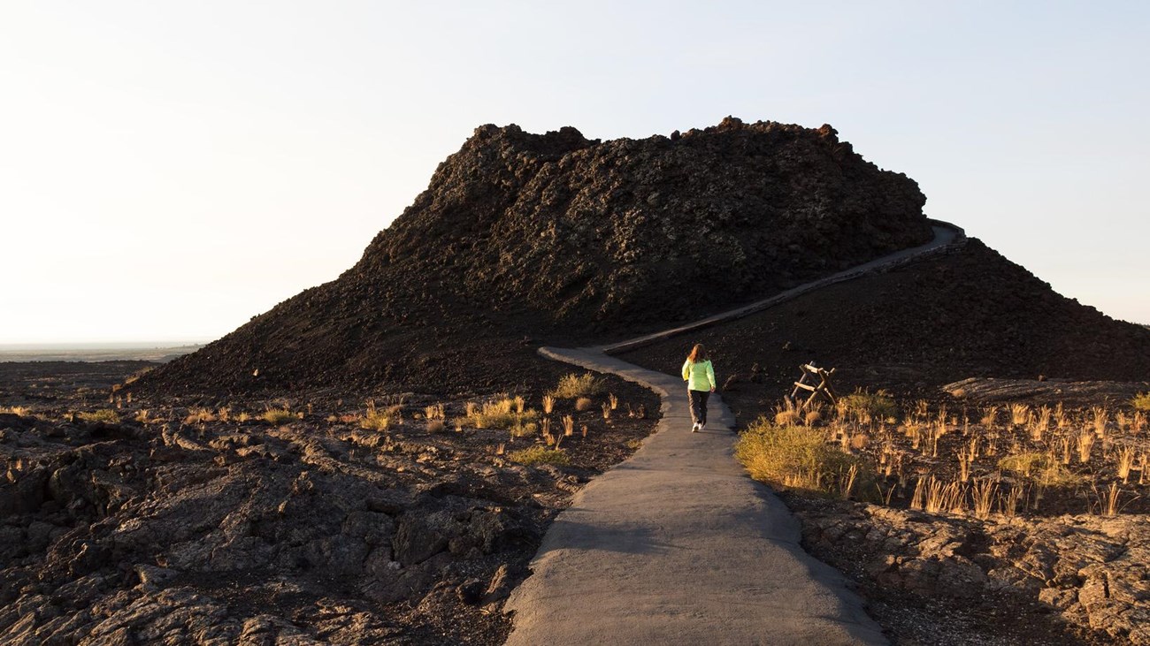 a person walking on a paved path up to a small volcanic cone